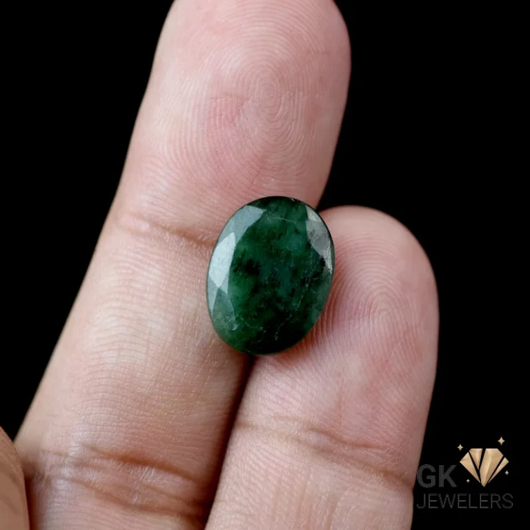 Oval-cut dark green emerald gemstone held between fingers
