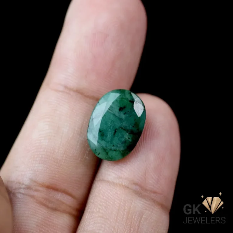 Oval-cut emerald gemstone held between fingers against a black background