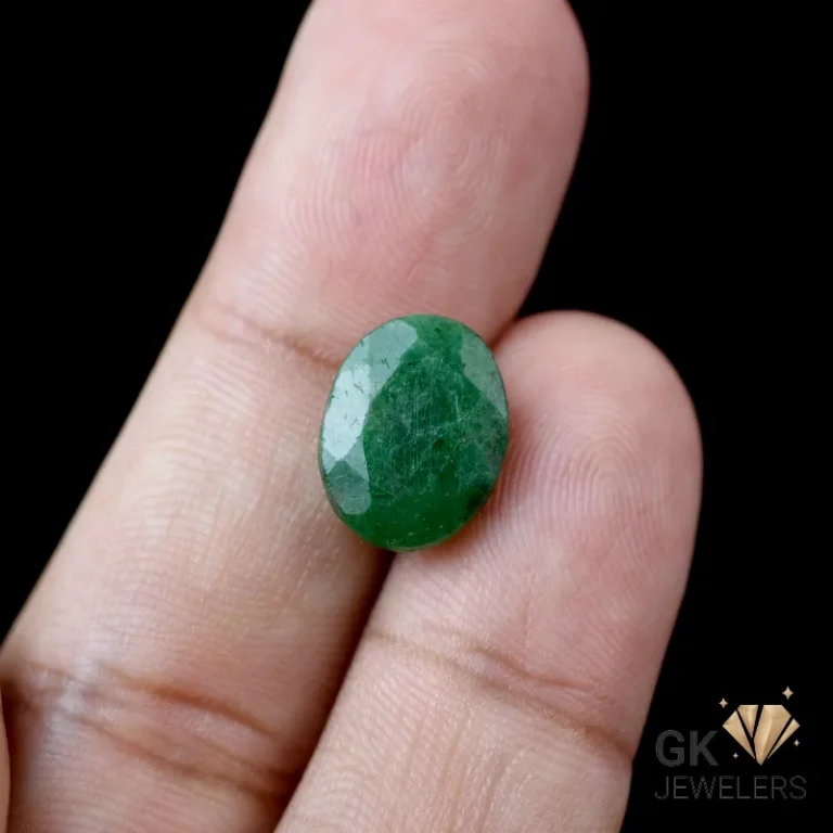 Faceted oval emerald gemstone held between human fingers