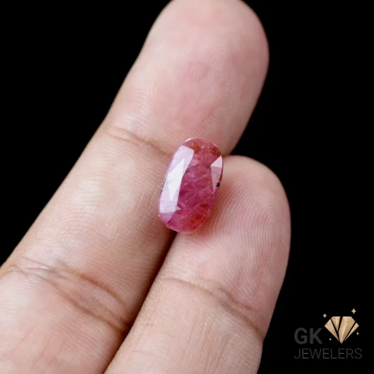 Pink ruby gemstone on a person's finger against a black backdrop