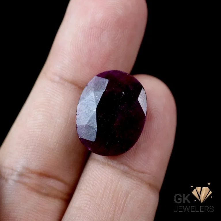 Deep red, round-cut garnet gemstone between fingers