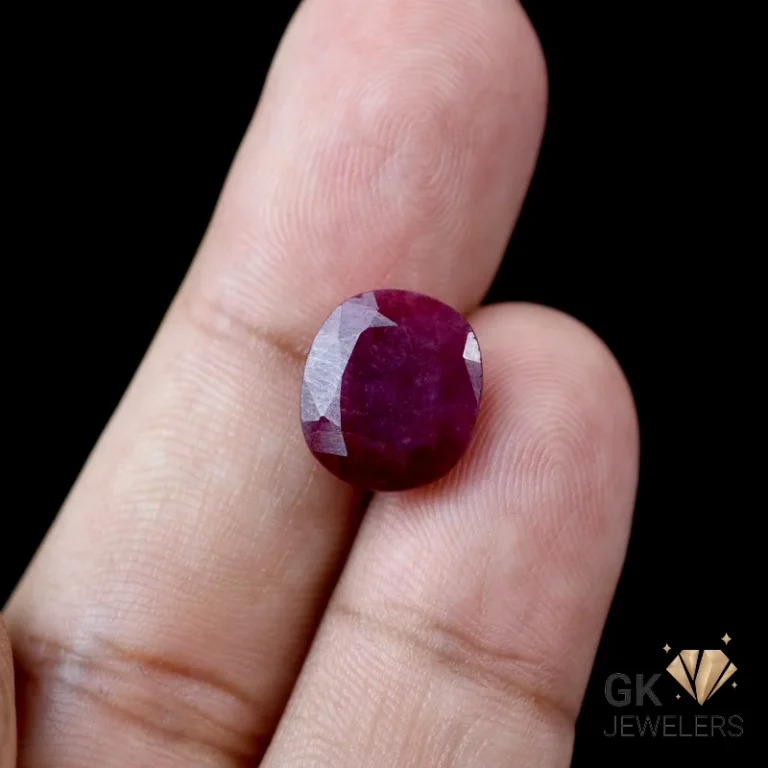 Oval ruby gemstone held between fingers, showcasing deep red color