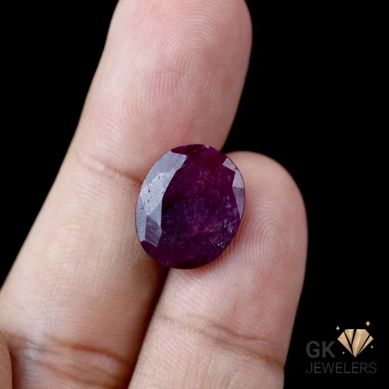 Ruby gemstone held between fingers, showcasing deep purple color and faceted cut