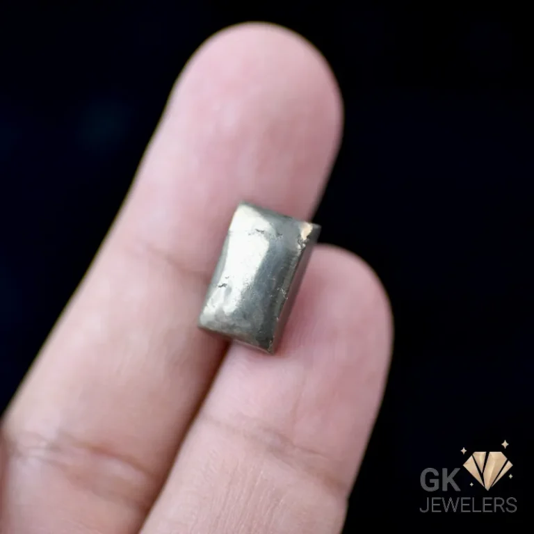 Silver cuboid earring held between fingers on a dark background