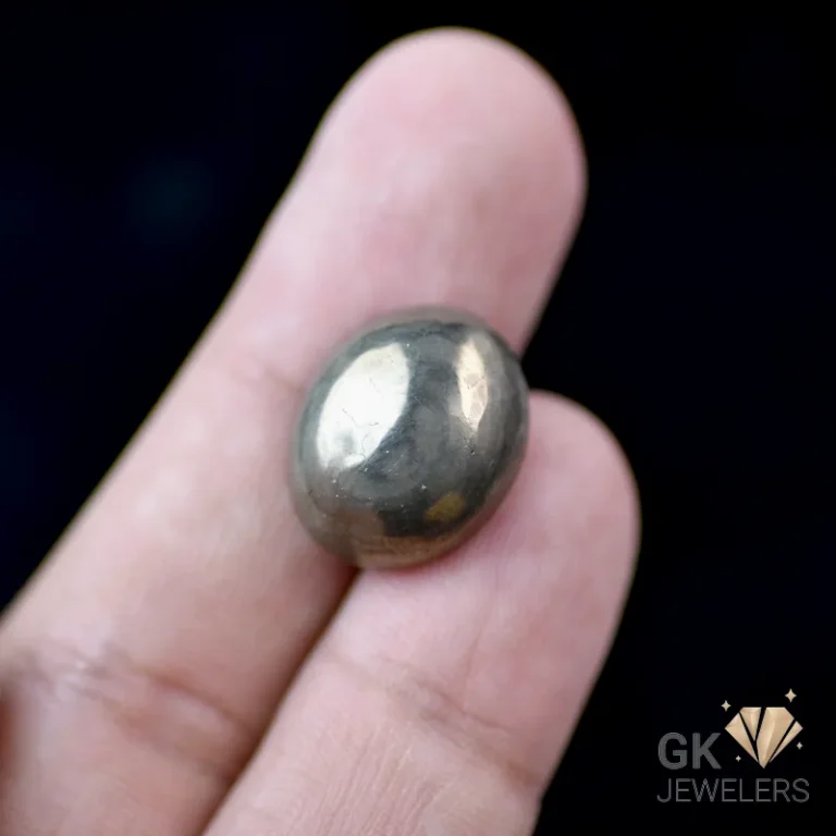 Polished round dark grey gemstone on human fingertips
