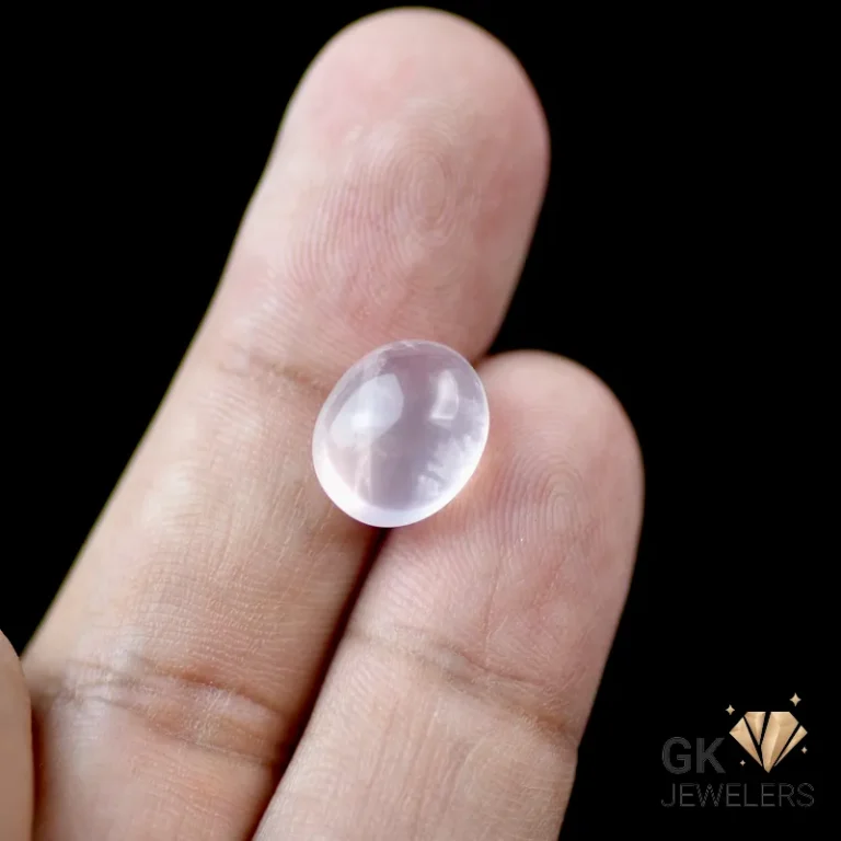 Rose quartz gemstone resting on fingertips against dark background