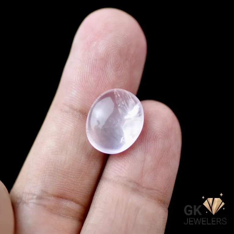 Rose quartz gemstone held between fingers, oval cut, pale pink hue