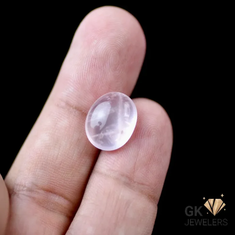 Hand holding a pale pink Rose Quartz gemstone with visible inclusions