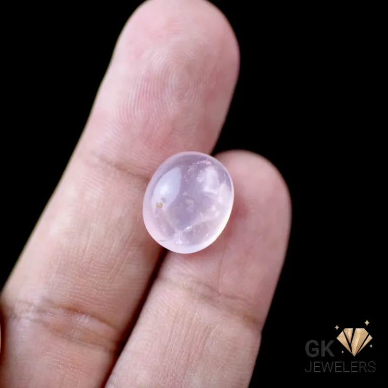 Pale pink rose quartz cabochon gemstone held between fingers