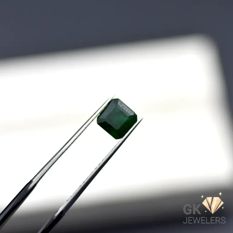 Emerald gemstone held by tweezers against a white background
