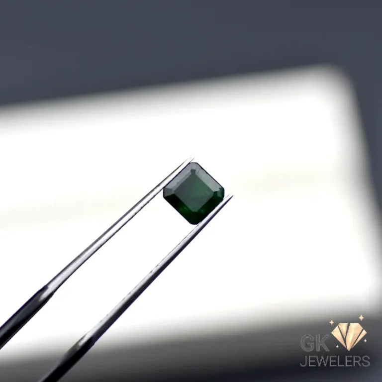 Emerald gemstone held by silver tweezers against a white background