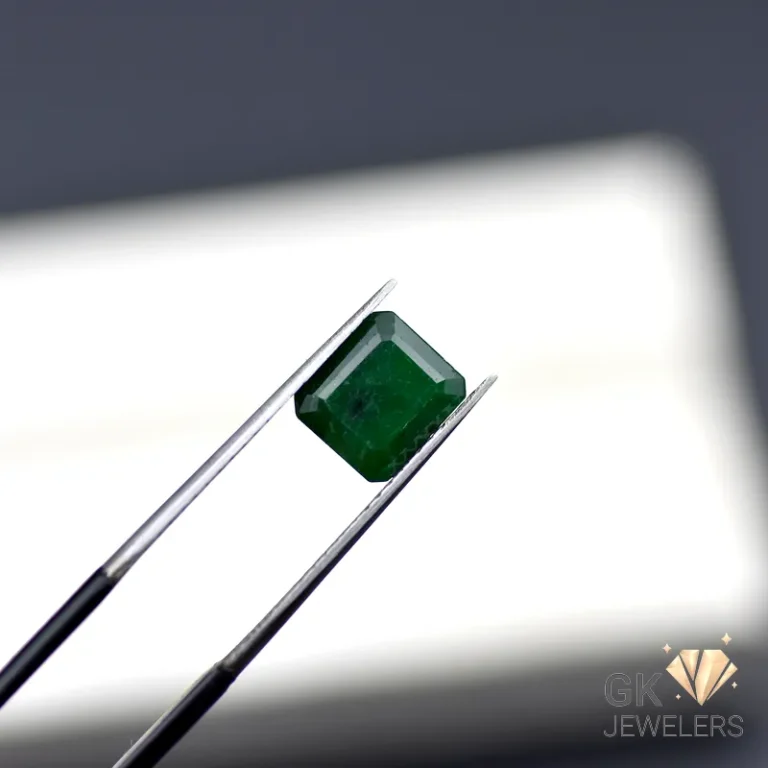 Emerald gemstone held by tweezers against a white background
