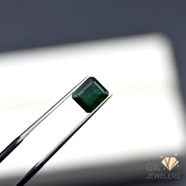 Emerald gemstone held by tweezers against a white background