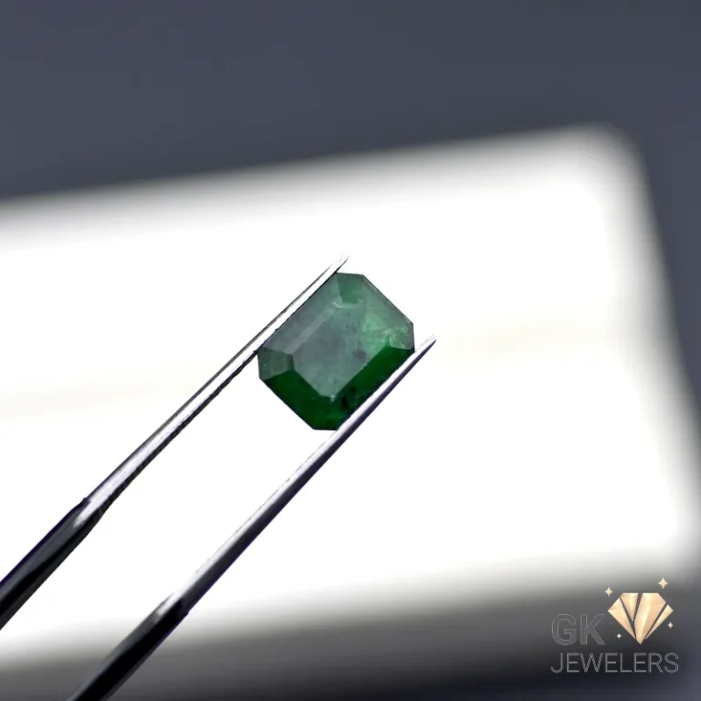 Emerald gemstone held by silver tweezers against a white background