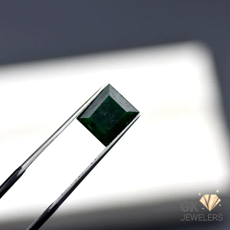 Emerald gemstone held by tweezers against a white background