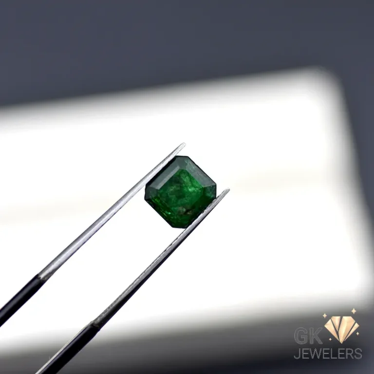 Emerald gemstone held by silver tweezers against a blurred white background