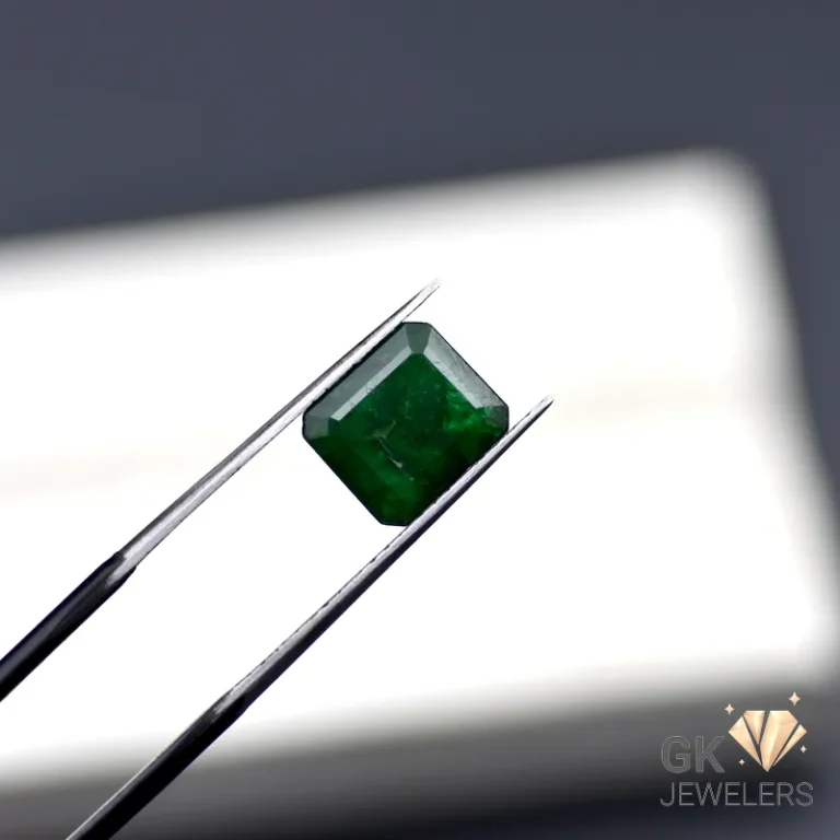 Emerald gemstone held by metal tweezers against a white background