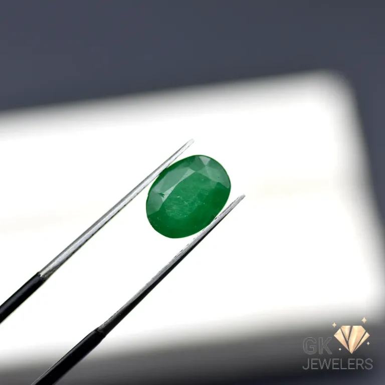 Oval-cut emerald gemstone held by tweezers on a white surface
