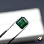 Emerald gemstone held by tweezers, showcasing deep green color and inclusions