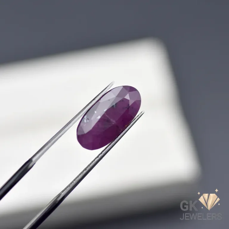 Oval-cut purple gemstone held by metal tweezers against a blurred white background