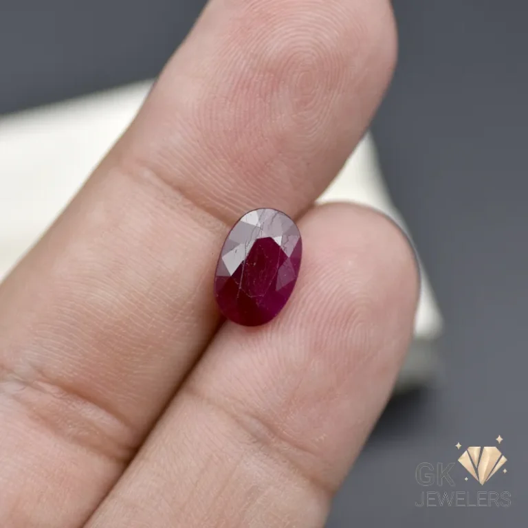 Ruby gemstone held between fingers on a gray surface