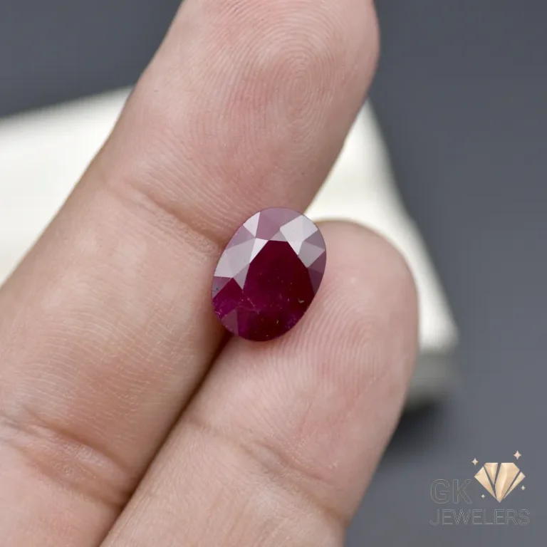 Oval-cut ruby gemstone held between fingers, showcasing its deep red color and faceted cut