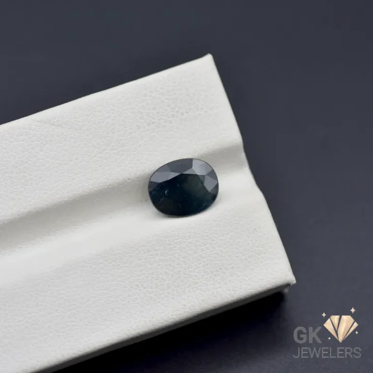 Oval-cut dark sapphire gemstone on white textured surface