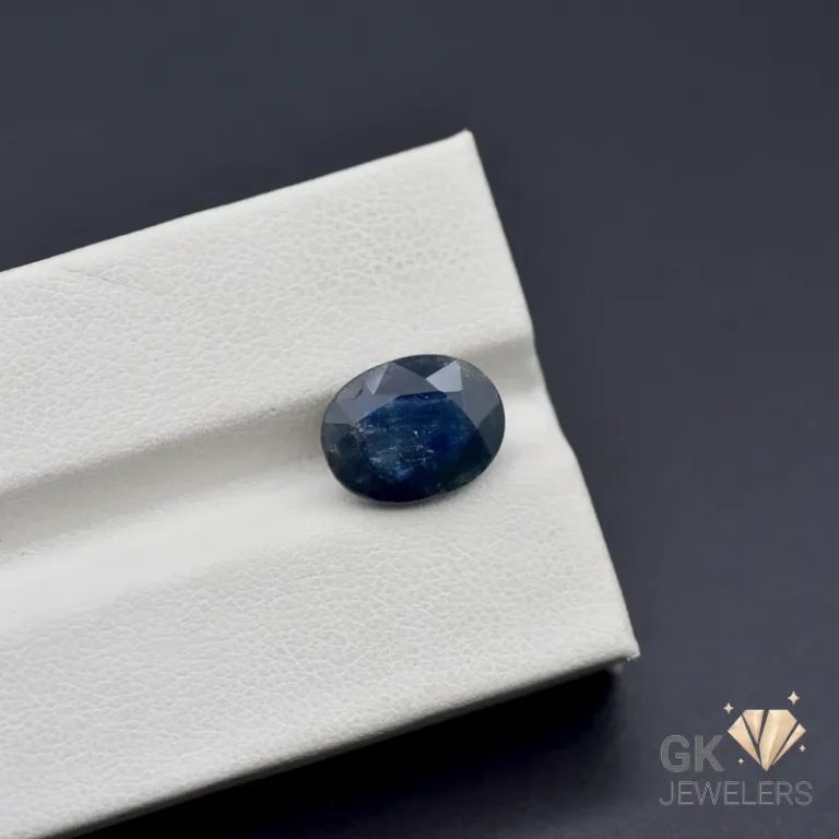 Oval-cut dark blue sapphire gemstone on a white textured surface