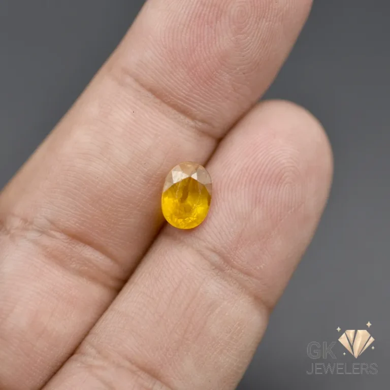 Oval-cut yellow gemstone on fingertips against a grey background