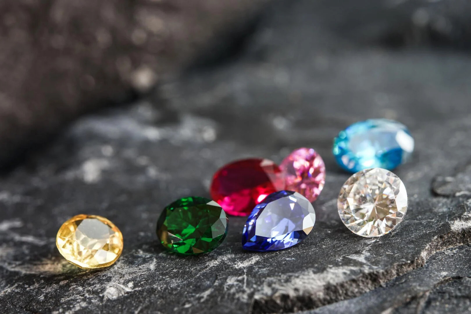 Colorful gemstones of various sizes on a dark gray stone surface, illustrating ring size variations for men and women in Pakistan