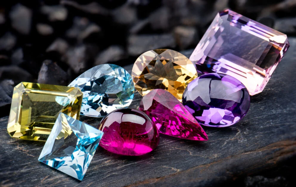 Assorted gemstones in various cuts and colors on dark surface, illustrating the importance of precise ring sizing for different stone shapes