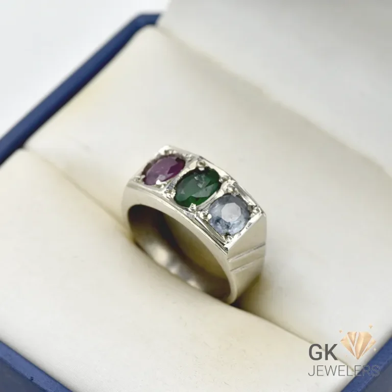 Silver ring featuring three oval-cut gemstones: ruby, emerald, and sapphire, in a handmade setting, displayed in a jewelry box