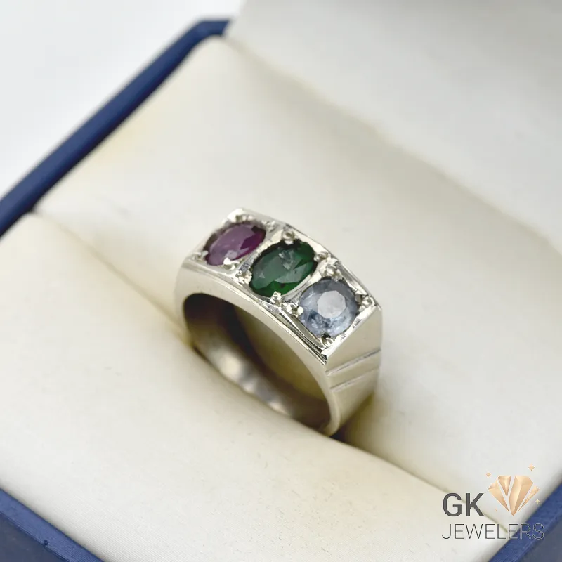 Silver ring featuring three oval-cut gemstones: ruby, emerald, and sapphire, in a handmade setting, displayed in a jewelry box
