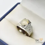 White sapphire gemstone set in a handmade silver ring with textured details, displayed in a cream-colored jewelry box