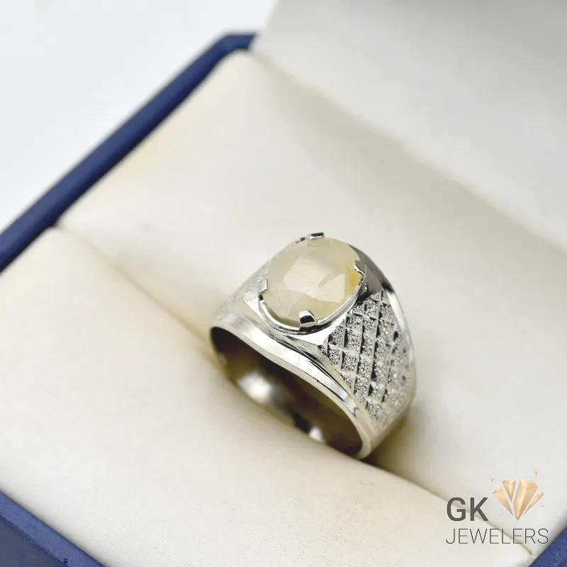 White sapphire gemstone set in a handmade silver ring with textured details, displayed in a cream-colored jewelry box