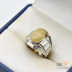 Silver ring featuring a large oval yellow gemstone in a handmade setting, displayed on white padding inside a blue jewelry box