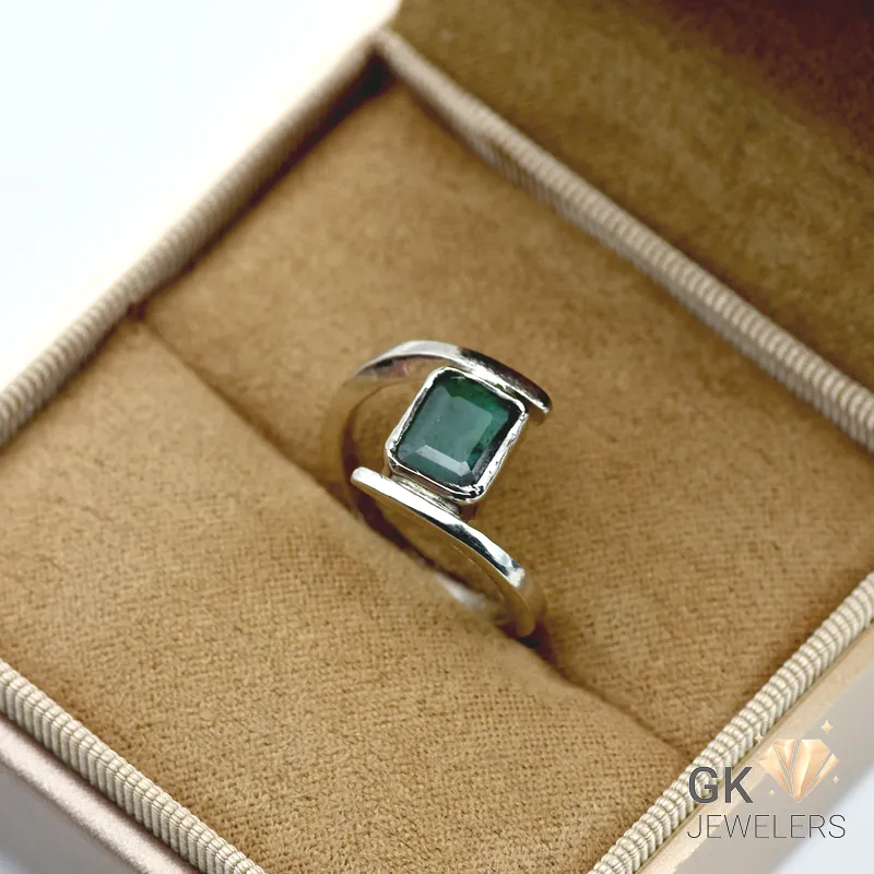 Silver ring with emerald-cut Zambian emerald gemstone in four-prong setting, displayed in a jewelry box with tan fabric lining