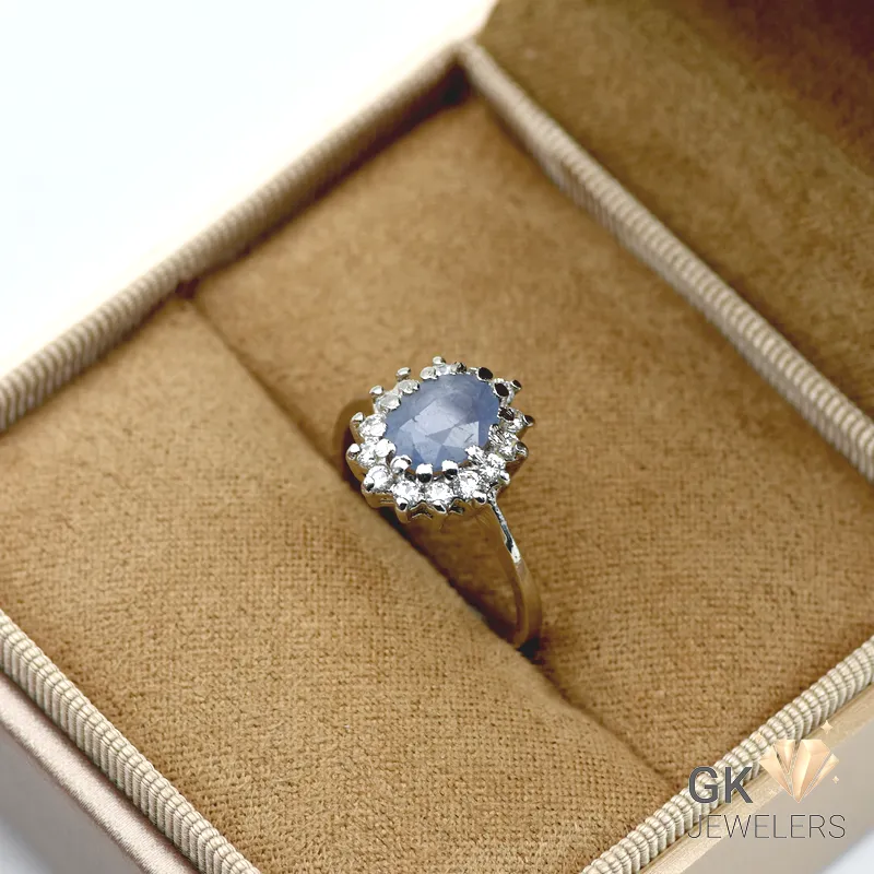 Oval blue sapphire gemstone surrounded by clear stones, set in sterling silver ring with handmade craftsmanship