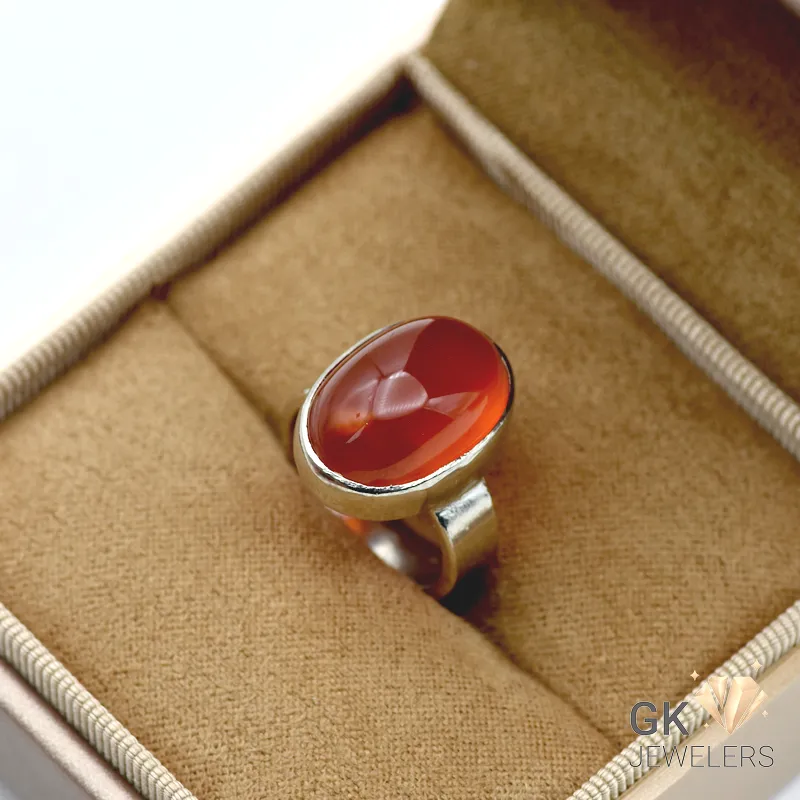 Red oval agate gemstone set in handmade 925 silver ring on beige jewelry box fabric