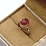 Red agate gemstone set in handmade silver ring, displayed on tan fabric in jewelry box