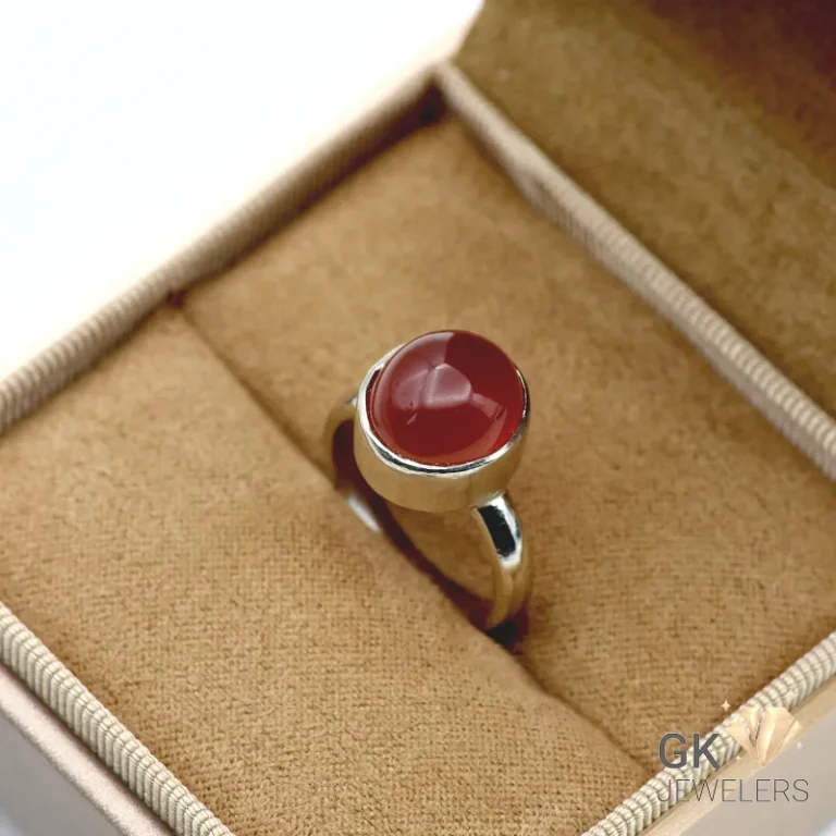 Red agate gemstone set in handmade silver ring, displayed on tan fabric in jewelry box