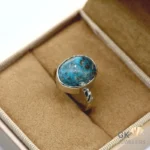 Oval-shaped turquoise gemstone set in a handmade silver ring, displayed in a jewelry box, showcasing its vibrant blue color and black matrix
