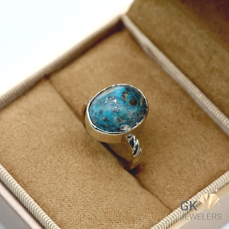 Oval-shaped turquoise gemstone set in a handmade silver ring, displayed in a jewelry box, showcasing its vibrant blue color and black matrix