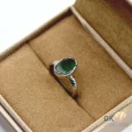 Oval-cut natural emerald gemstone set in a handmade 925 silver ring on a beige fabric display