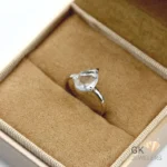 Pear-shaped transparent aquamarine gemstone set in handmade silver ring, displayed in a tan jewelry box