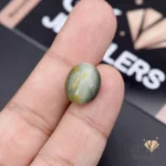 Hand holding a 10.30ct green catseye gemstone from Africa, showcasing its opaque structure and silky band