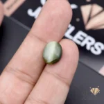 Hand holding an 8.10ct opaque green catseye gemstone from Africa, showcasing its chatoyant effect