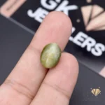 Oval-shaped green catseye gemstone held between fingers, showcasing chatoyancy effect