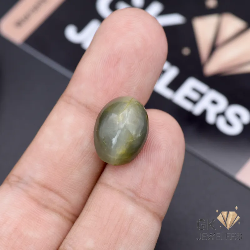 Oval green catseye gemstone held between fingers, showcasing chatoyancy and opaque transparency