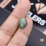 Oval-cut green catseye gemstone held between fingers, showcasing its opaque transparency and silky luster